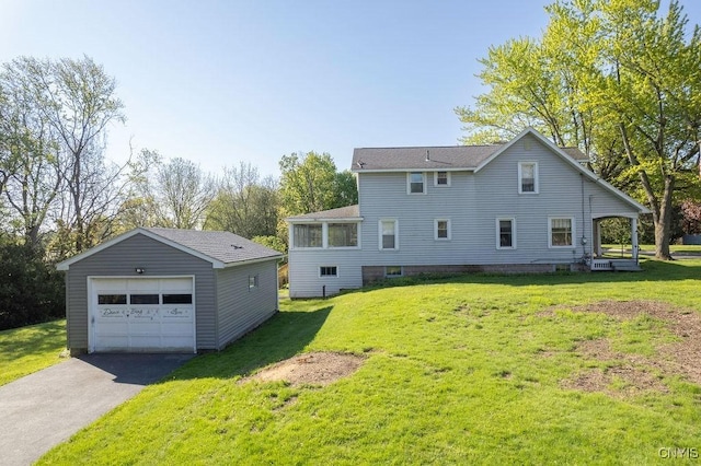 rear view of house with an outdoor structure, a detached garage, asphalt driveway, and a yard