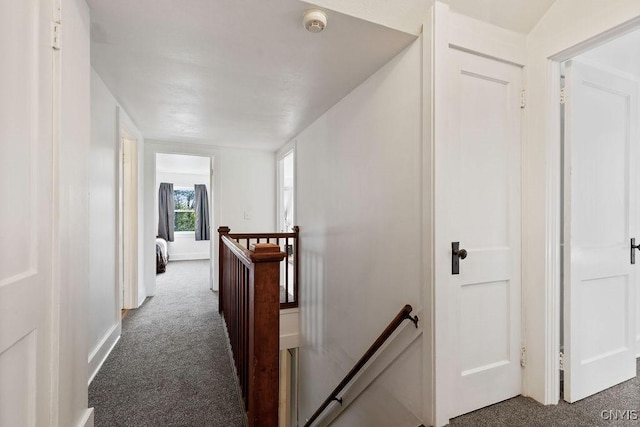 hallway featuring an upstairs landing, dark colored carpet, and baseboards