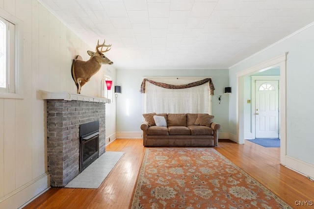 living room featuring light wood finished floors, a brick fireplace, ornamental molding, and baseboards
