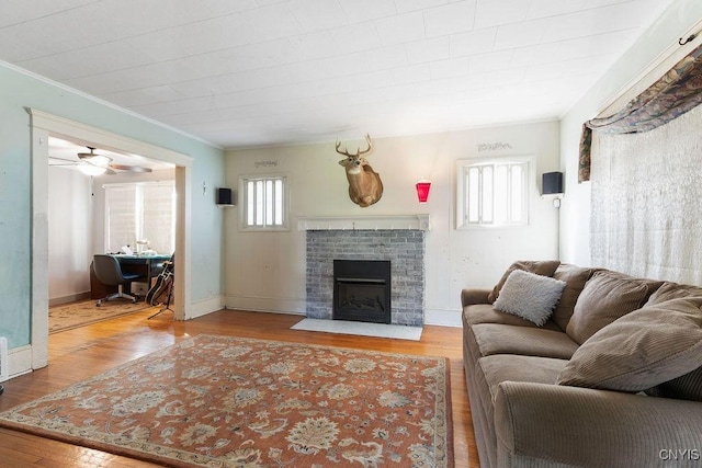 living area featuring ornamental molding, wood finished floors, a brick fireplace, a ceiling fan, and baseboards