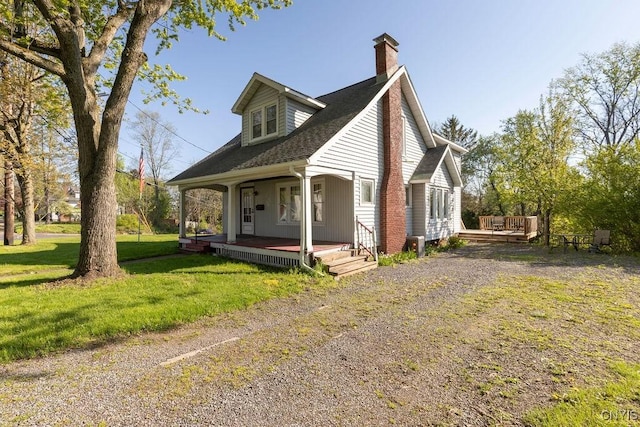 view of front of property with covered porch, a chimney, a front lawn, and a shingled roof