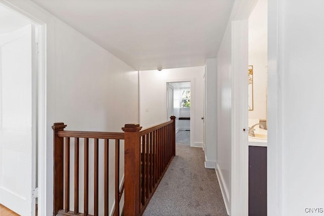 hallway featuring an upstairs landing, carpet floors, and baseboards