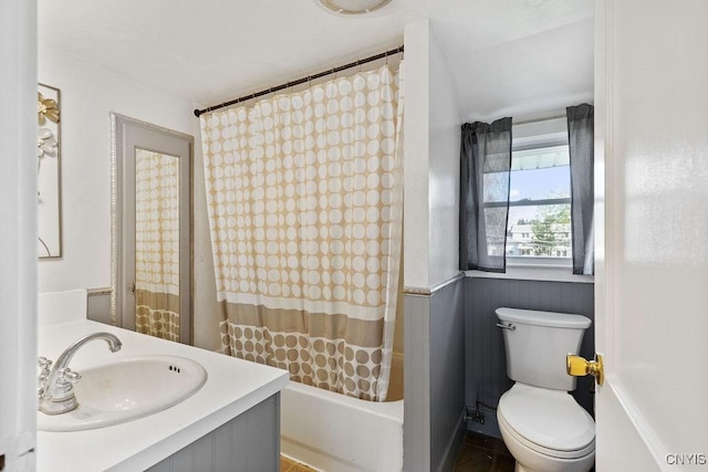 full bath with toilet, vanity, shower / bath combination with curtain, and a wainscoted wall