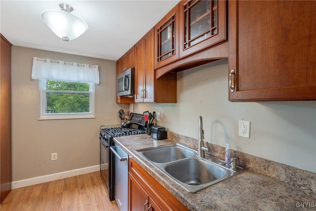 kitchen with a sink, appliances with stainless steel finishes, light wood-style flooring, glass insert cabinets, and brown cabinetry