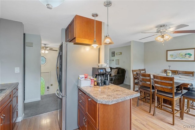 kitchen featuring a ceiling fan, light wood-style floors, light countertops, freestanding refrigerator, and brown cabinets
