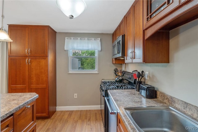 kitchen featuring appliances with stainless steel finishes, a sink, brown cabinetry, and light wood-style flooring