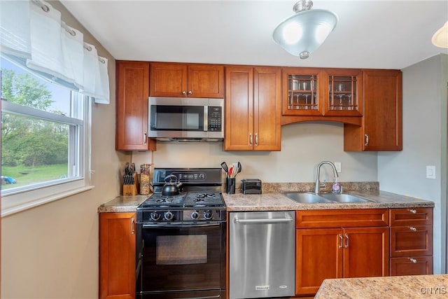 kitchen with stainless steel appliances, a sink, brown cabinetry, and glass insert cabinets