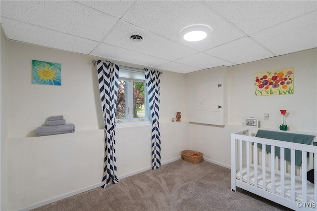 carpeted bedroom with a drop ceiling, baseboards, and a crib