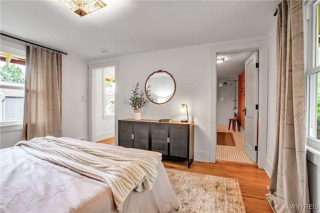 bedroom with light wood-style flooring, baseboards, and ensuite bath