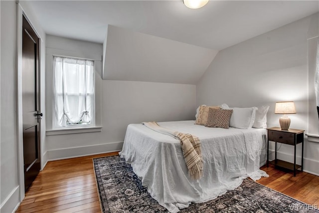 bedroom with wood finished floors, baseboards, and vaulted ceiling