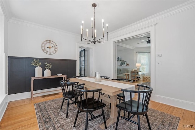 dining area featuring light wood-type flooring, ornamental molding, a chandelier, and wainscoting