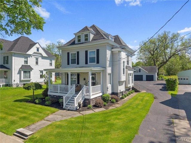 american foursquare style home with a porch, a detached garage, a front lawn, and an outdoor structure