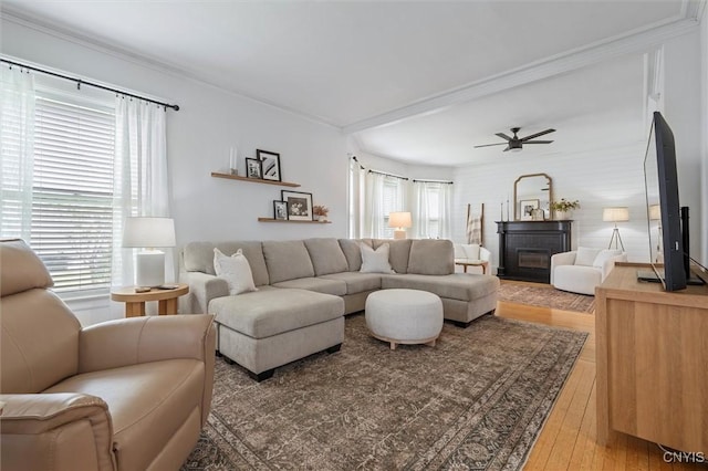 living room featuring a ceiling fan, a fireplace, wood-type flooring, and ornamental molding
