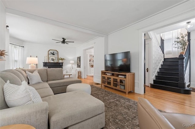 living room featuring light wood-type flooring, stairway, ceiling fan, and ornamental molding