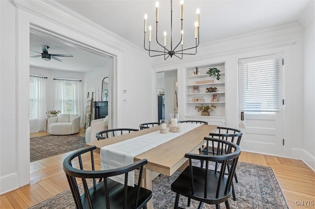 dining room featuring a chandelier, ceiling fan, built in features, ornamental molding, and light wood finished floors