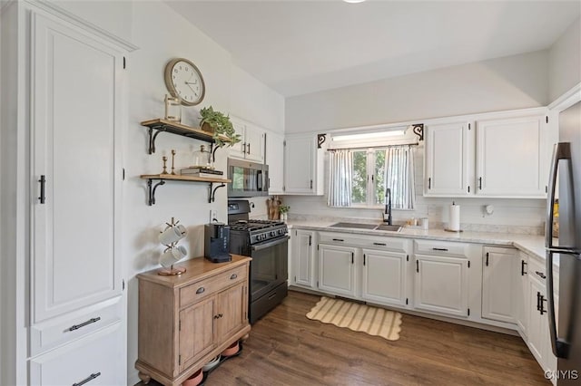 kitchen with appliances with stainless steel finishes, a sink, white cabinetry, dark wood-type flooring, and open shelves