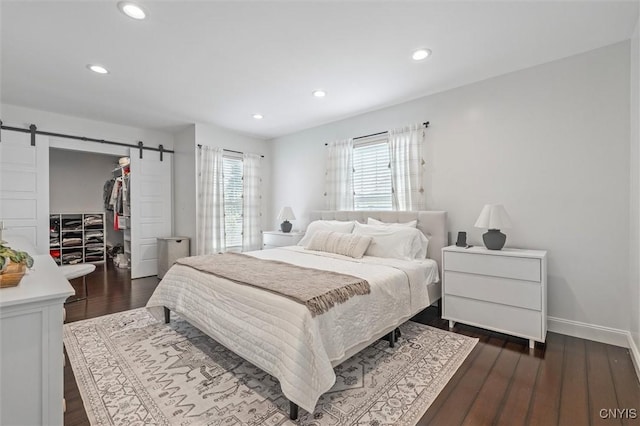 bedroom featuring a barn door, dark wood-style flooring, a walk in closet, recessed lighting, and a closet