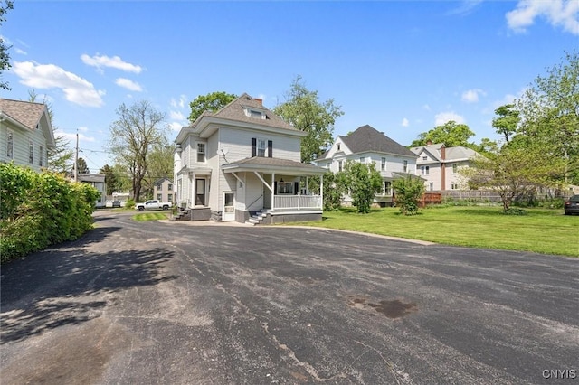 view of front of home featuring covered porch, a front yard, a residential view, and driveway