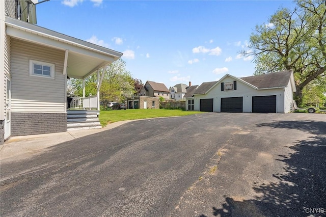 view of side of home featuring a garage, asphalt driveway, a residential view, an outdoor structure, and a yard