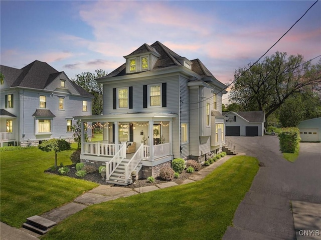 traditional style home featuring a porch, a garage, an outbuilding, and a front yard