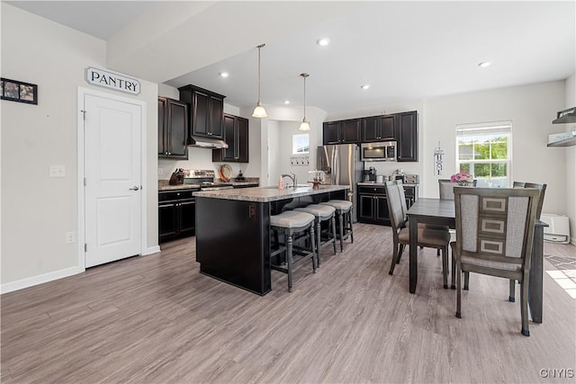 kitchen with stainless steel appliances, a kitchen breakfast bar, light wood-type flooring, light countertops, and a kitchen island with sink