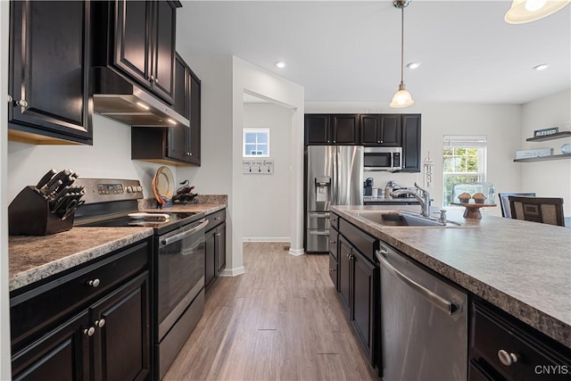 kitchen with appliances with stainless steel finishes, a sink, light wood-style flooring, hanging light fixtures, and under cabinet range hood