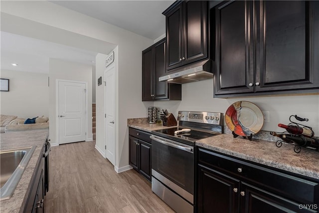 kitchen featuring stainless steel electric stove, under cabinet range hood, a sink, light wood-style flooring, and dark cabinetry