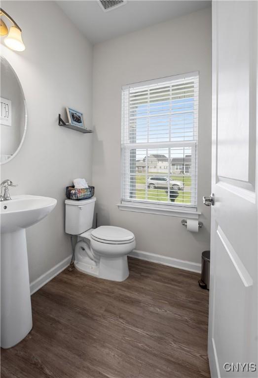 half bath with baseboards, toilet, wood finished floors, and a sink