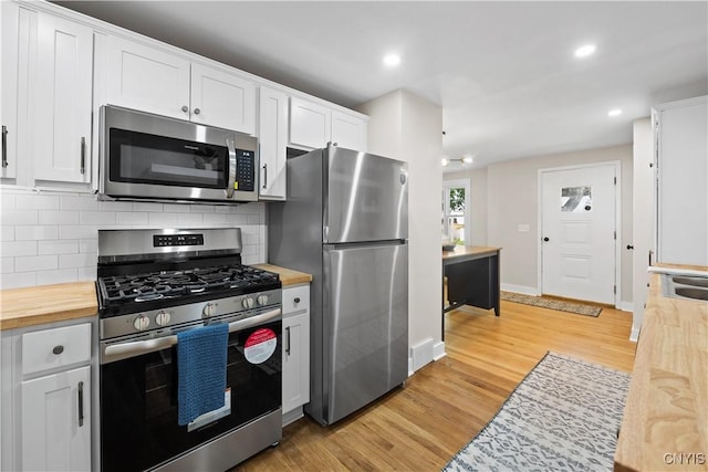 kitchen featuring appliances with stainless steel finishes, butcher block counters, backsplash, light wood-style flooring, and white cabinetry