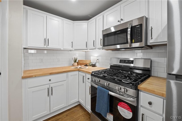 kitchen with wood counters, appliances with stainless steel finishes, decorative backsplash, white cabinetry, and dark wood finished floors