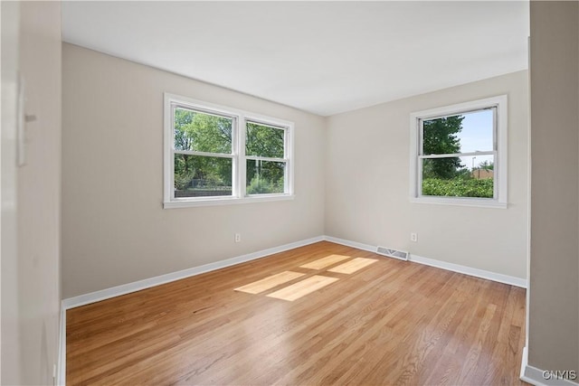 empty room featuring healthy amount of natural light, wood finished floors, and baseboards
