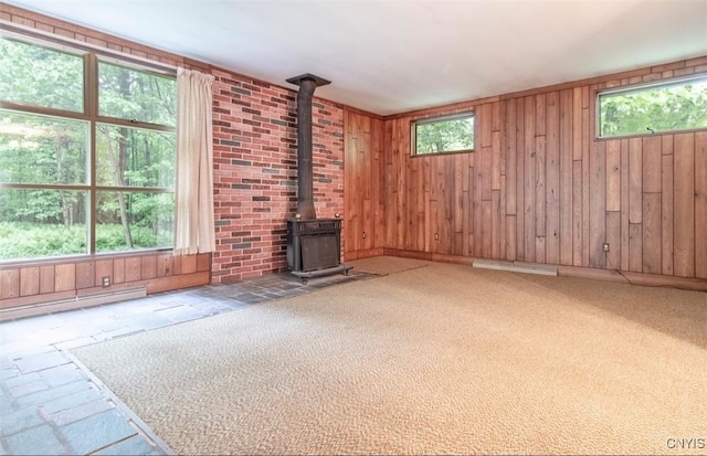 115 Stafford Dr, Rutland, NY 13612 - unfurnished living room with a wood stove, plenty of natural light, wood walls, baseboard heating, and carpet flooring