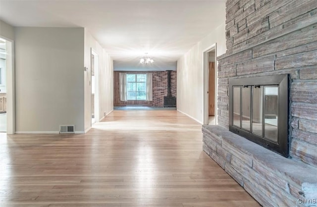 115 Stafford Dr, Rutland, NY 13612 - unfurnished living room with a stone fireplace, wood finished floors, a chandelier, baseboards, and a wood stove