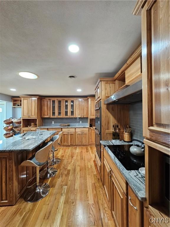 5813 Grace Rd, Deerfield, NY 13502 - kitchen featuring extractor fan, a kitchen bar, light wood-type flooring, stone countertops, and open shelves