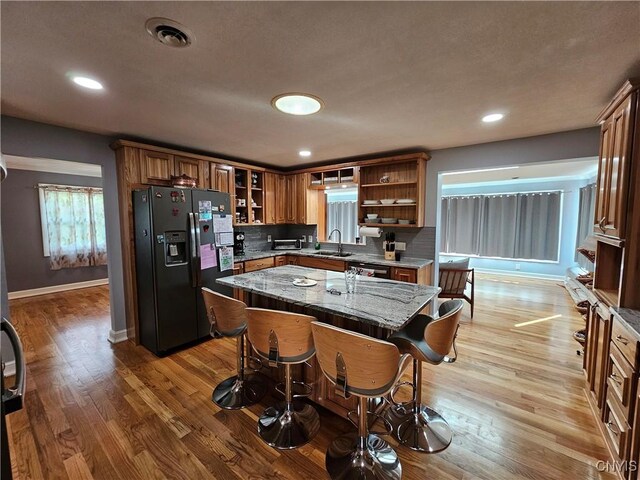 5813 Grace Rd, Deerfield, NY 13502 - kitchen featuring black refrigerator with ice dispenser, open shelves, a sink, light wood-style floors, and light stone counters
