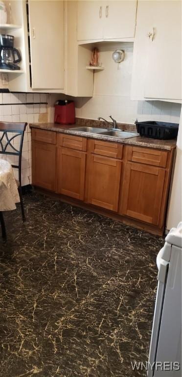 kitchen with a sink, stove, backsplash, dark countertops, and brown cabinets