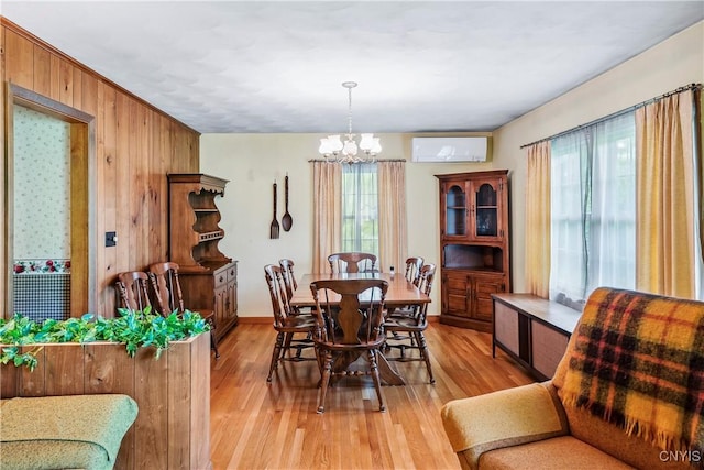 dining space with a chandelier, a wall mounted air conditioner, light wood-style flooring, wooden walls, and baseboards