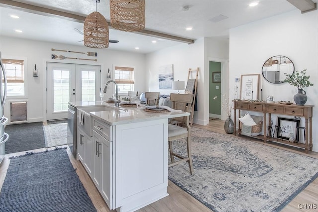 26618 Three Mile Point Rd, Lyme, NY 13622 - kitchen featuring stainless steel dishwasher, beam ceiling, a breakfast bar area, a kitchen island with sink, and a sink