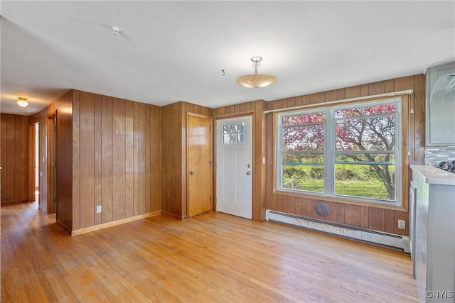 foyer entrance with a baseboard radiator, light wood-type flooring, and wood walls