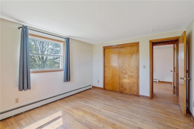unfurnished bedroom featuring baseboard heating, light wood finished floors, a closet, and baseboards