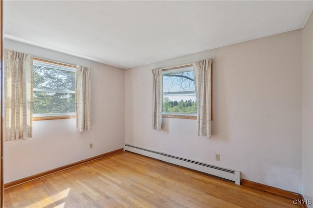 empty room with a baseboard heating unit, light wood-style floors, and baseboards