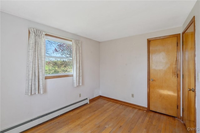 spare room with baseboard heating, light wood-type flooring, and baseboards