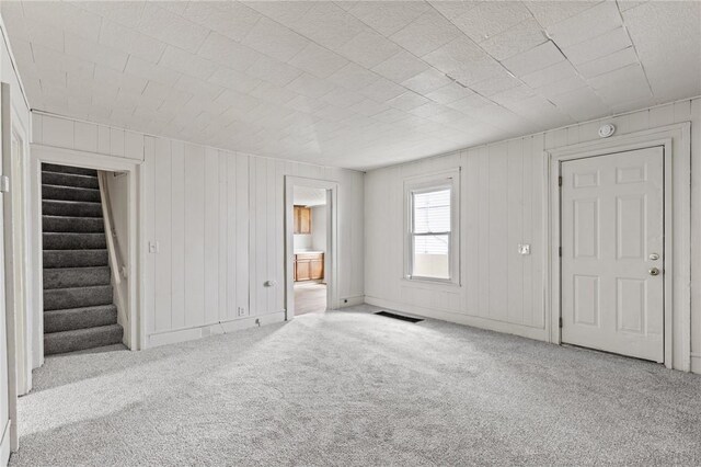 unfurnished living room with carpet flooring, stairs, and wood walls