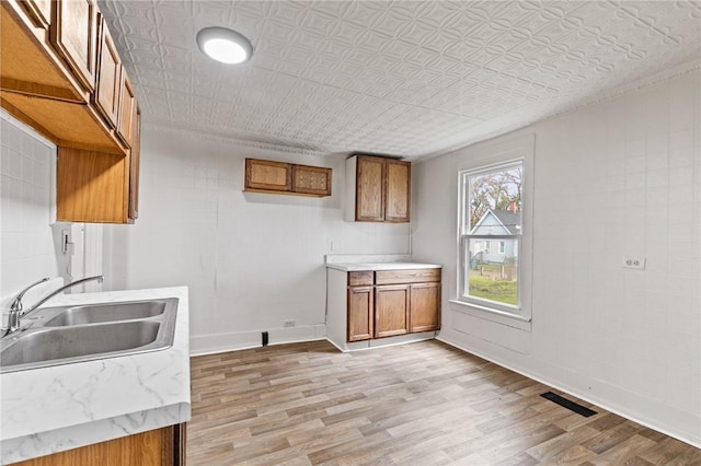 clothes washing area featuring an ornate ceiling, light wood finished floors, baseboards, a sink, and crown molding