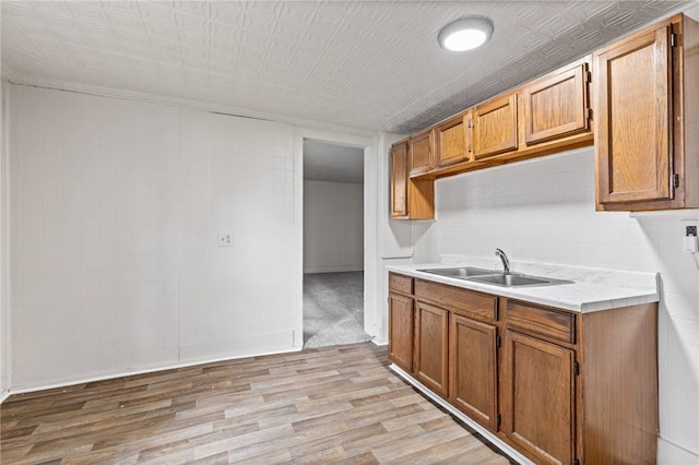 kitchen featuring a sink, light countertops, light wood-style flooring, and brown cabinetry