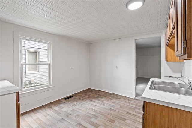 kitchen with a sink, brown cabinets, plenty of natural light, light wood-style flooring, and an ornate ceiling