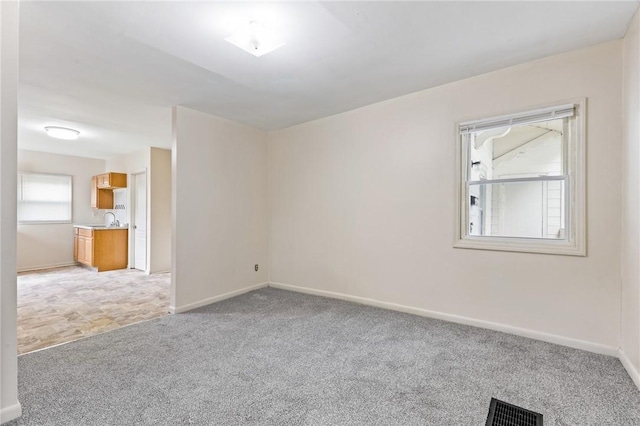 empty room featuring light colored carpet, baseboards, and a sink