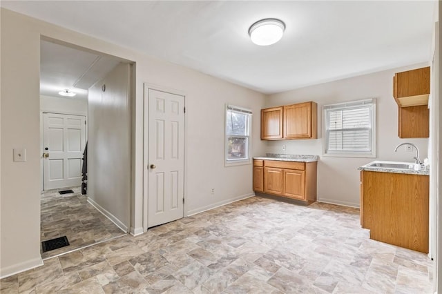 kitchen featuring stone finish floors, light countertops, a sink, and baseboards