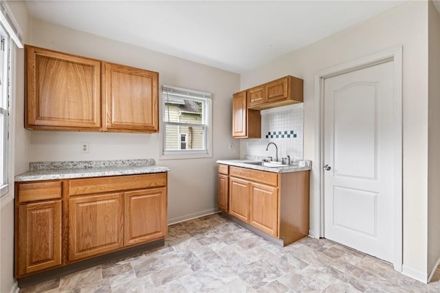 kitchen featuring a sink, light countertops, baseboards, decorative backsplash, and stone finish floors