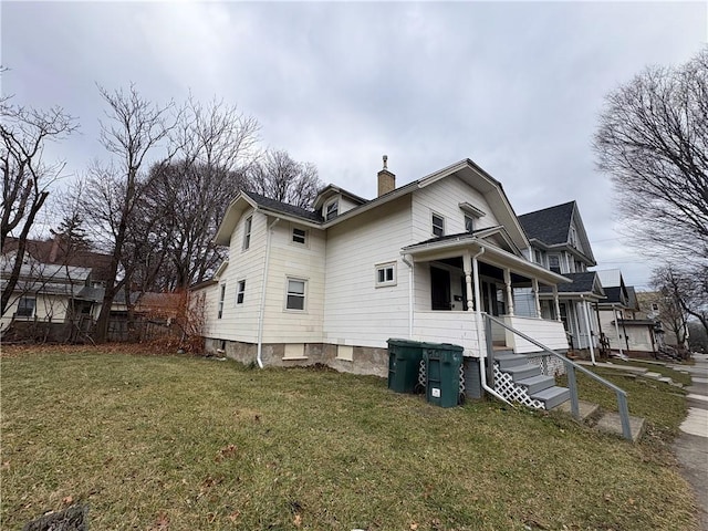 view of side of property with a chimney, a lawn, and covered porch